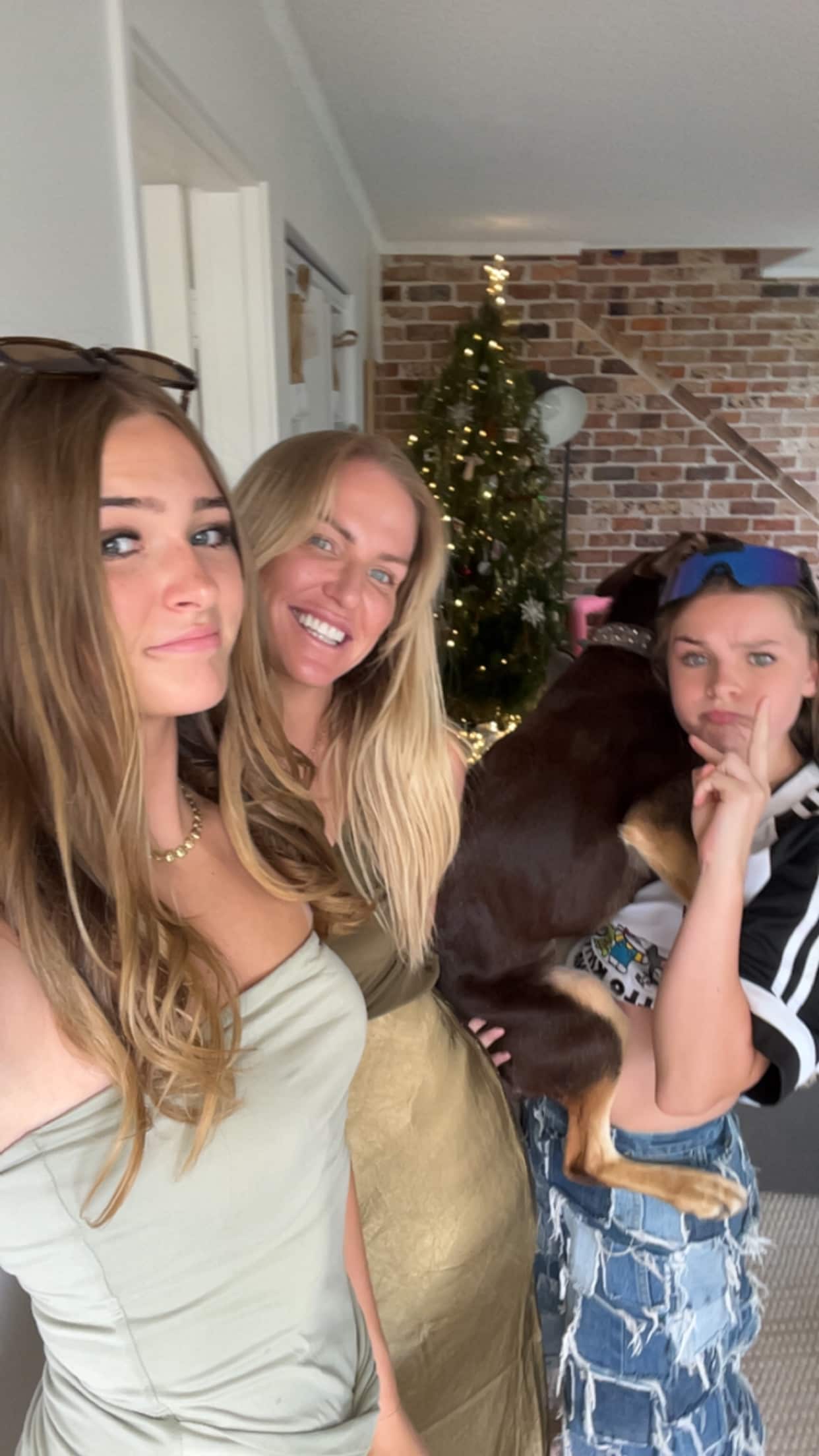 Two daughters are either side of their mother as they pose for a selfie with a Christmas tree behind them