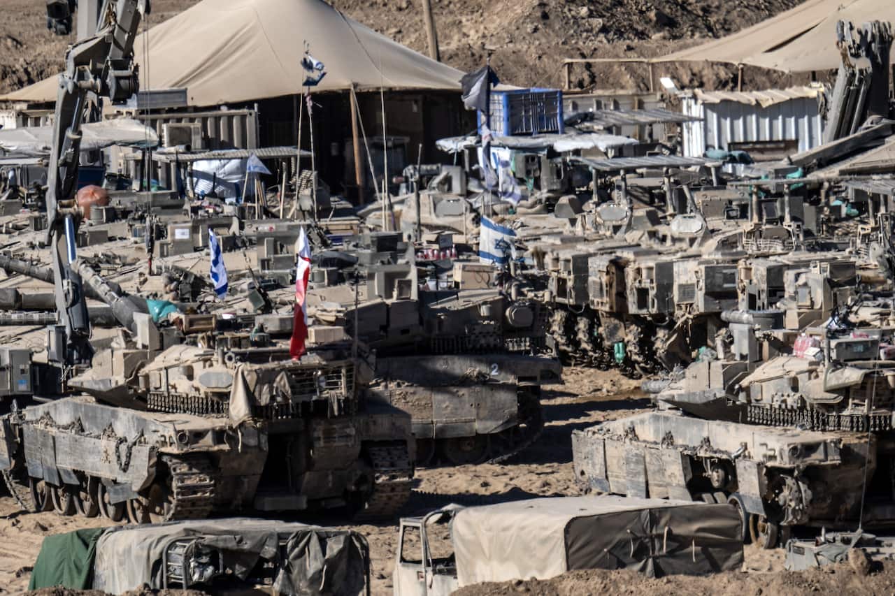 Military tanks and vehicles, some with Israeli flags, parked beside each other.
