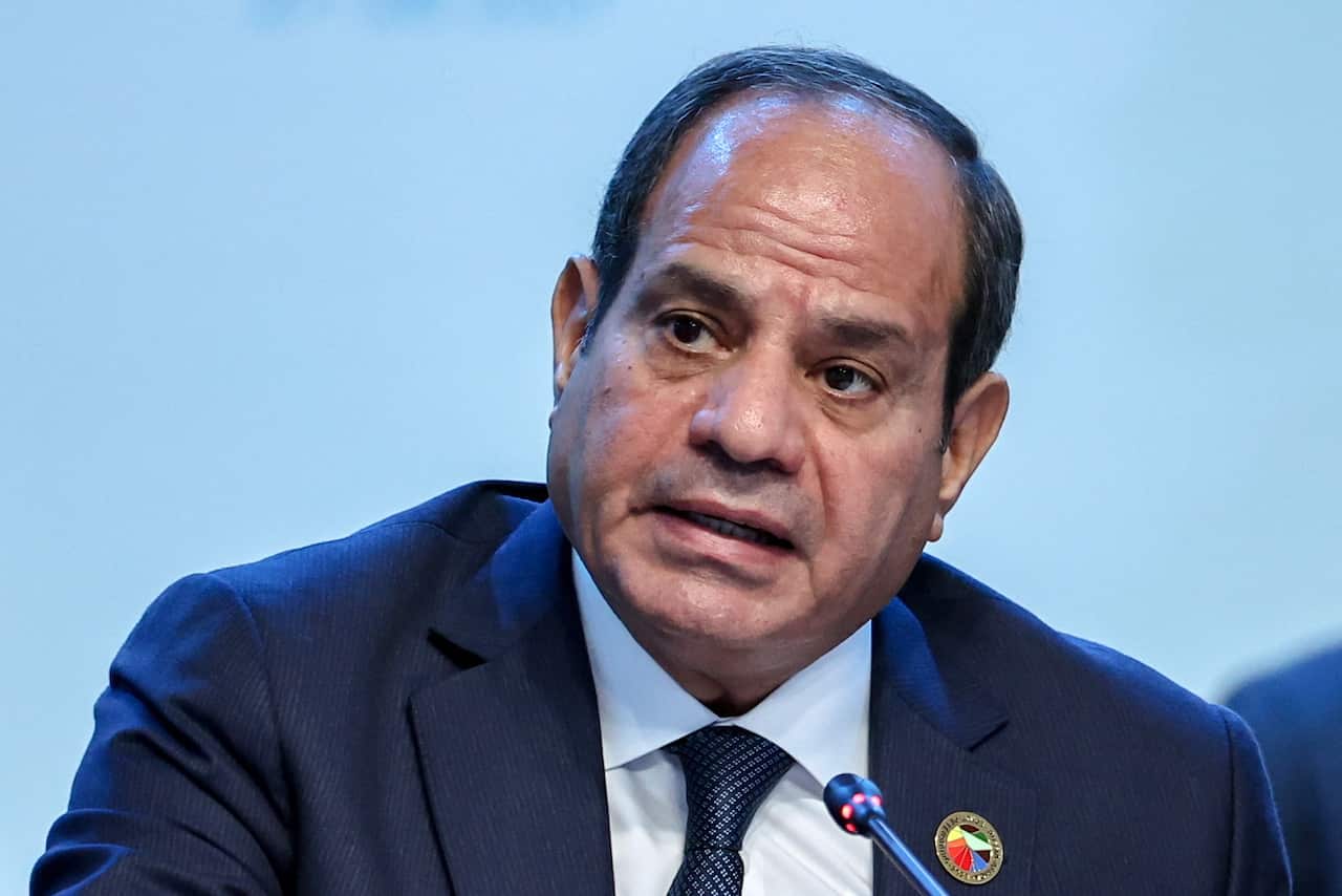 Close-up of man in blue suit speaking with his cocked to the side, with a serious expression. 