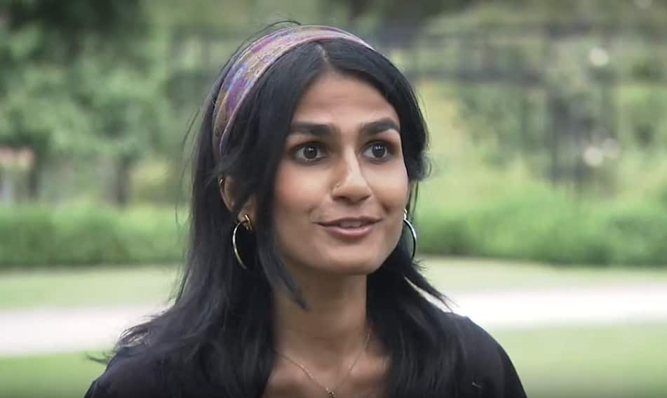 Woman with black hair and brown skin wears gold hoop earrings and a purple and yellow headband