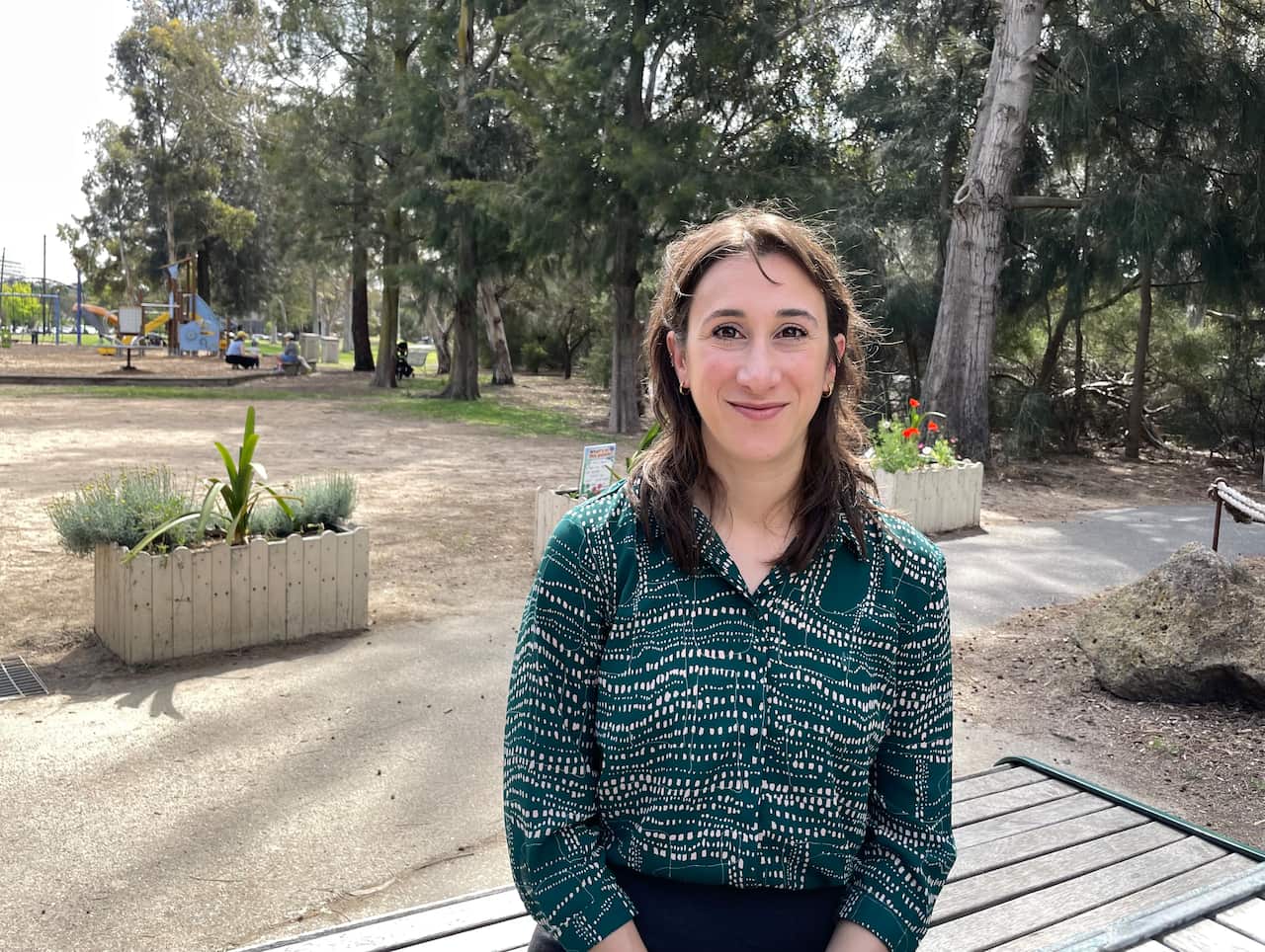 Uma mulher com uma camisa verde e branca parada em um parque sorri.