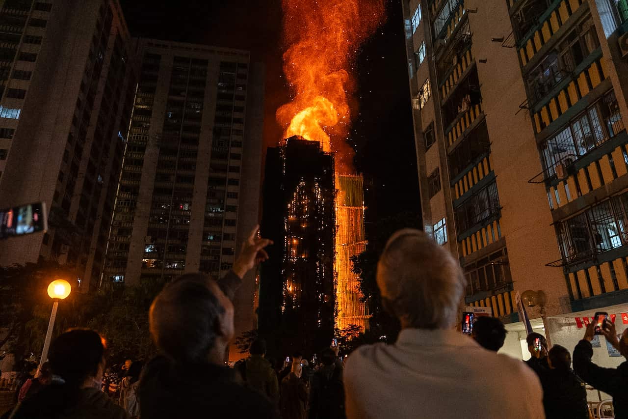People on the ground looking up and watching as a building is engulfed in flames.