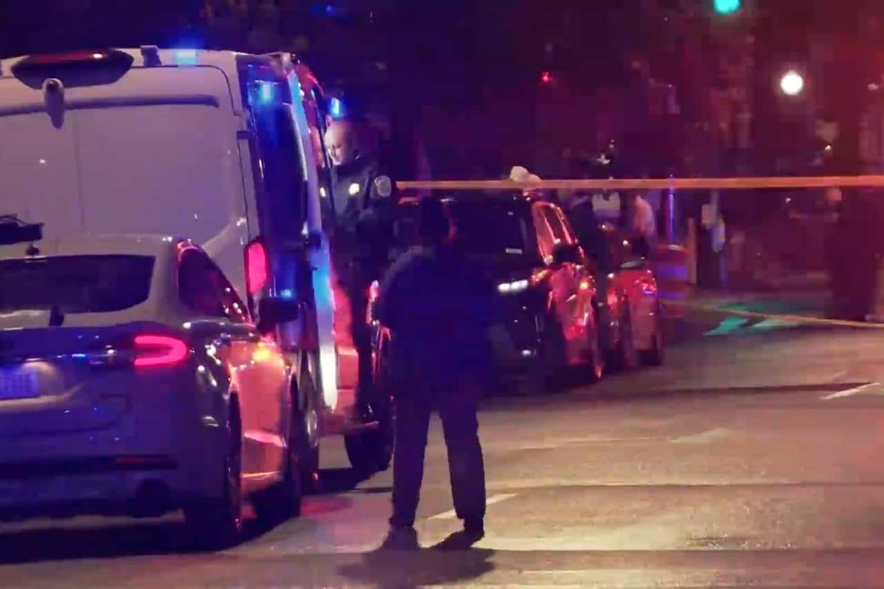 A person standing on a road, near police vehicles and police tape.
