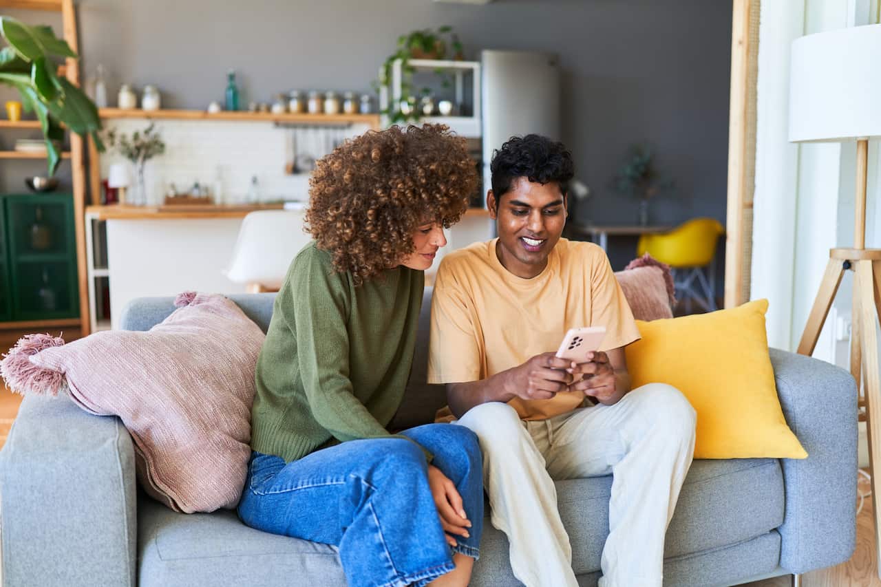 Multiracial couple sitting on the couch happily watching a mobile phone screen