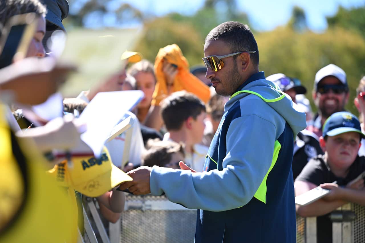 A man wearing a blue zipper is signing autographs for young children.