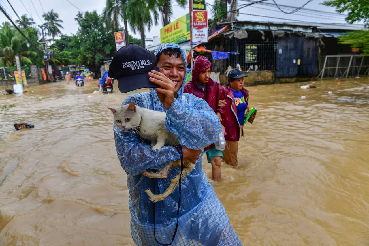 A Vietnamese man carrying a cat through flood waters