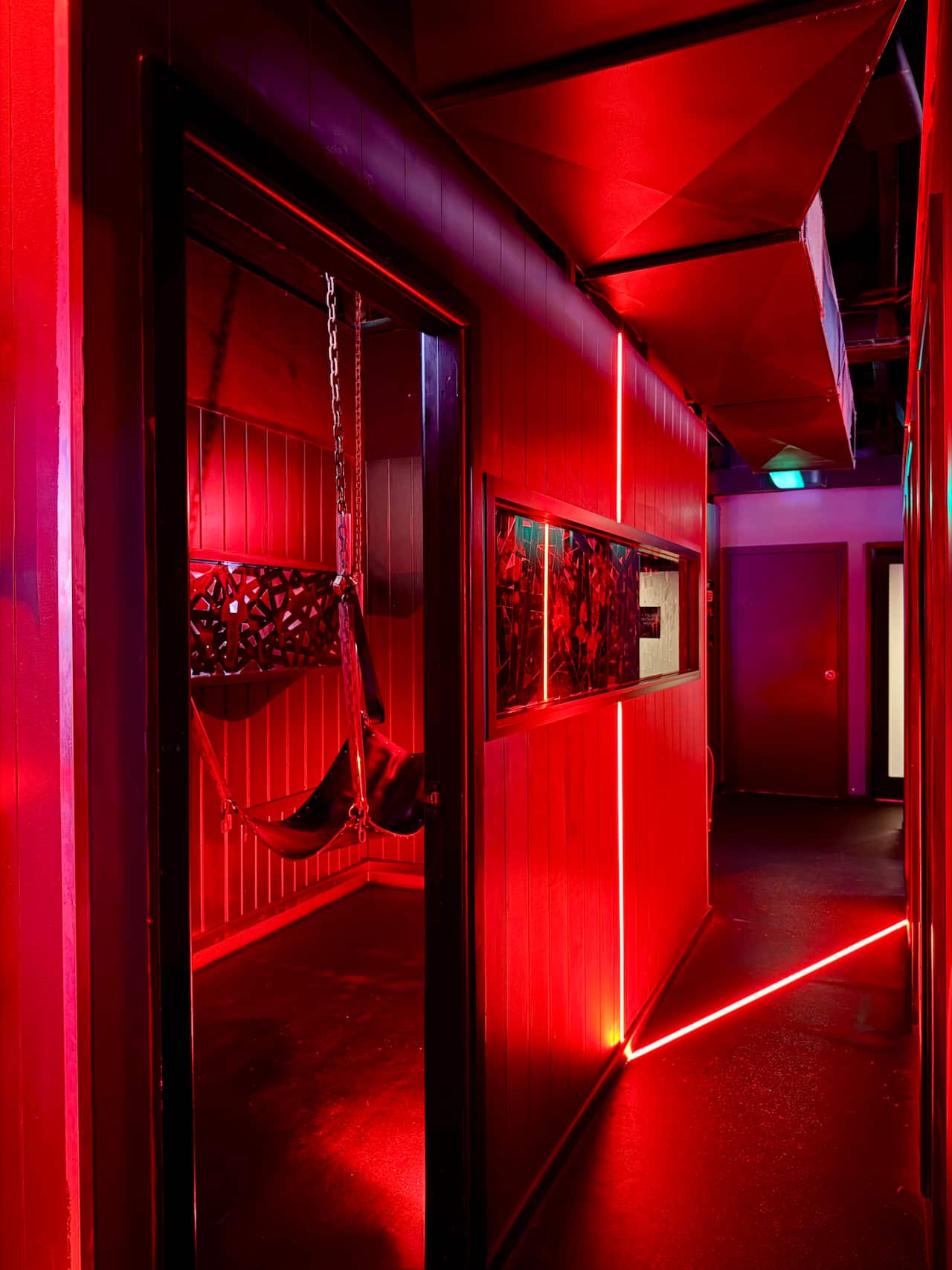 An interior shot of a sex swing in a red neon-lit room inside Sauna X by 357.