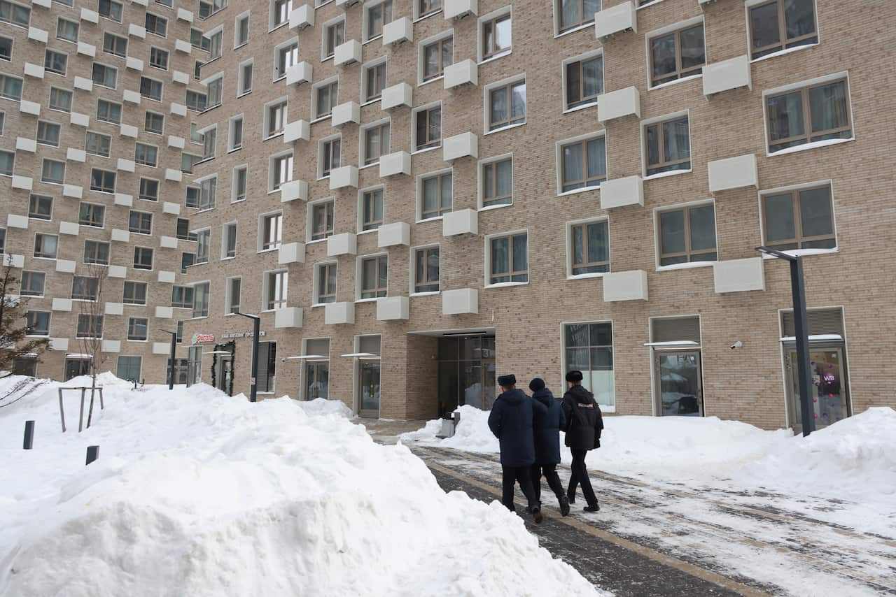 The entrance to a multi-storey apartment block surrounded by deep snow. Three police officers dressed in black are also pictured. 
