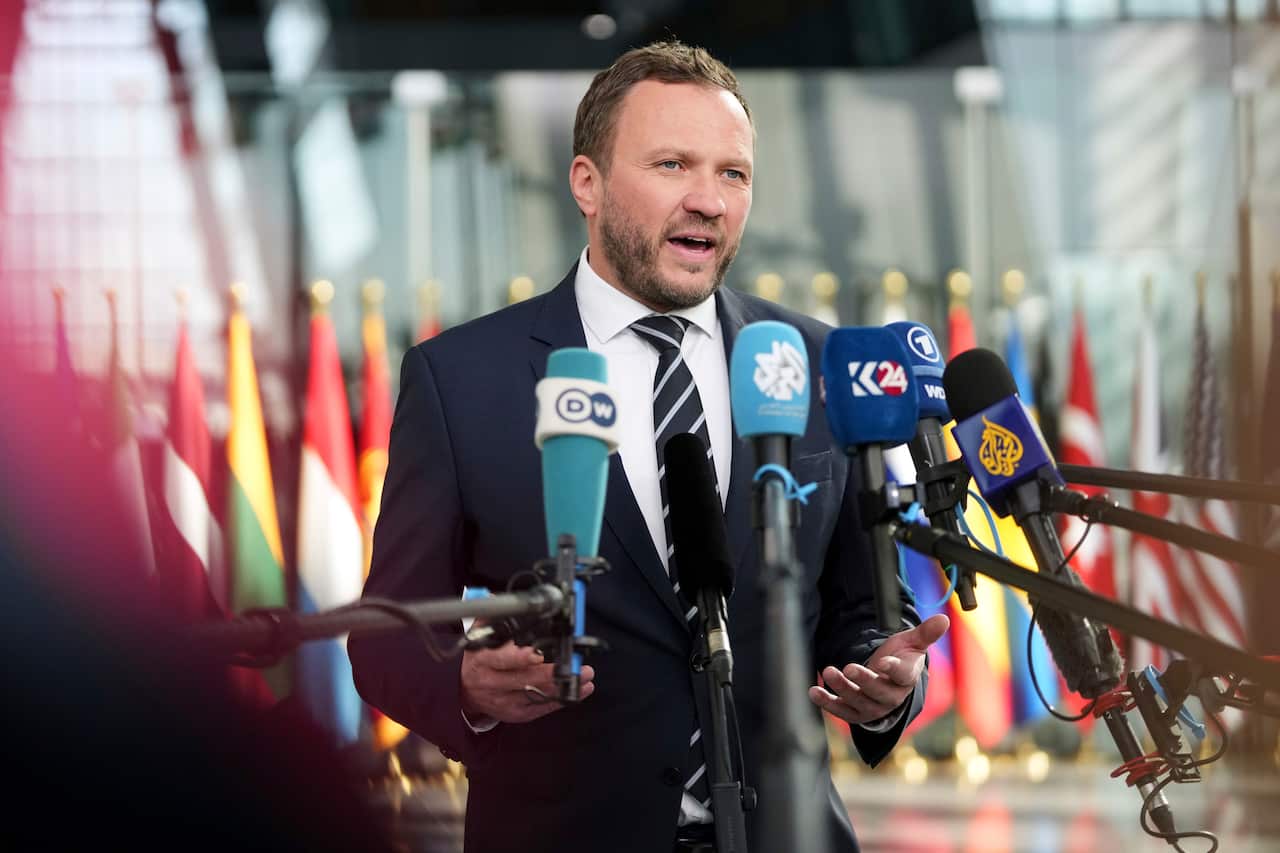 A middle-aged white man speaking in front of several microphones.