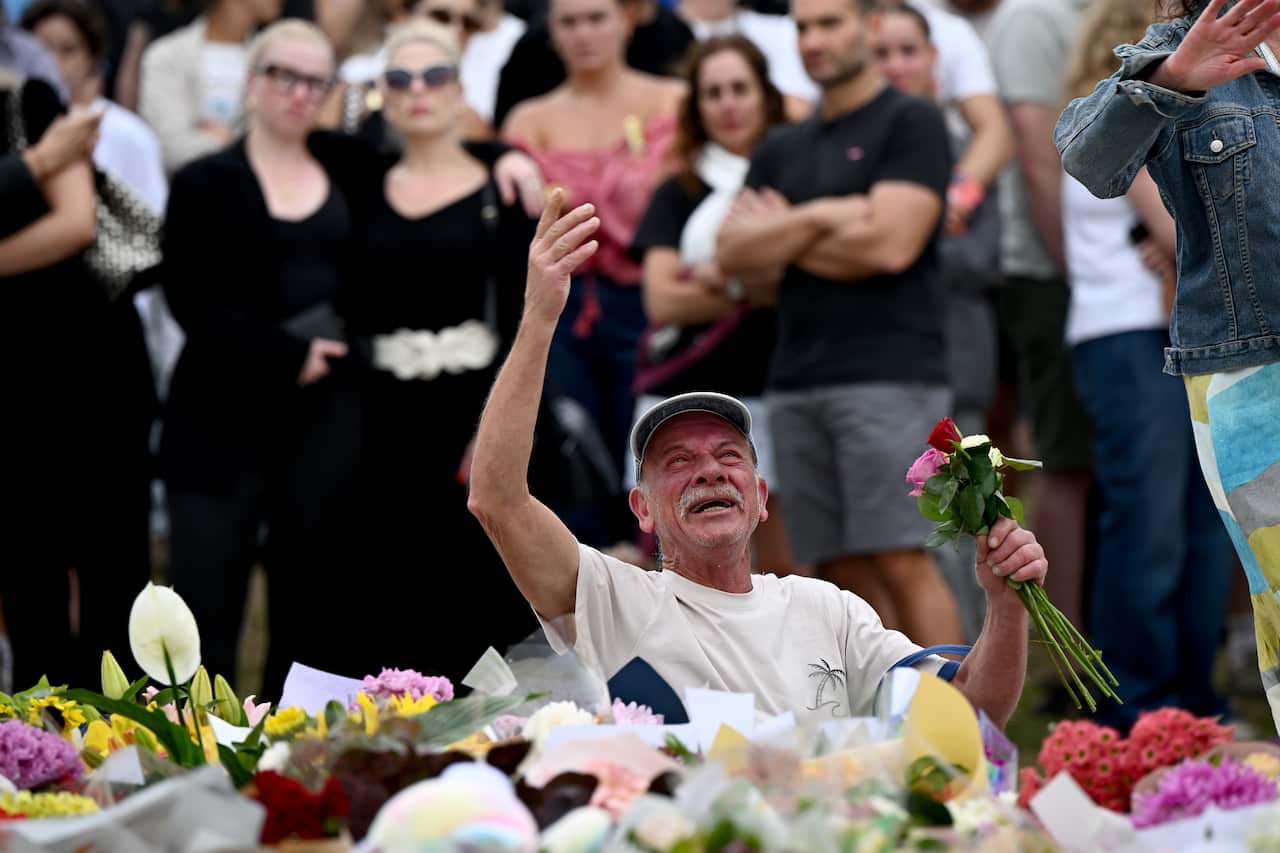 Mourner cries and stretches his hand in the air as he lays flowers at a vigil.