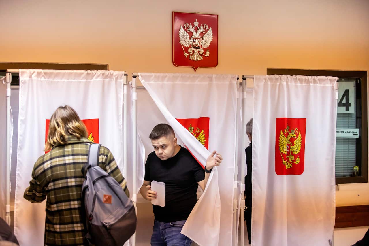 People enter and exit polling booths with white curtains.