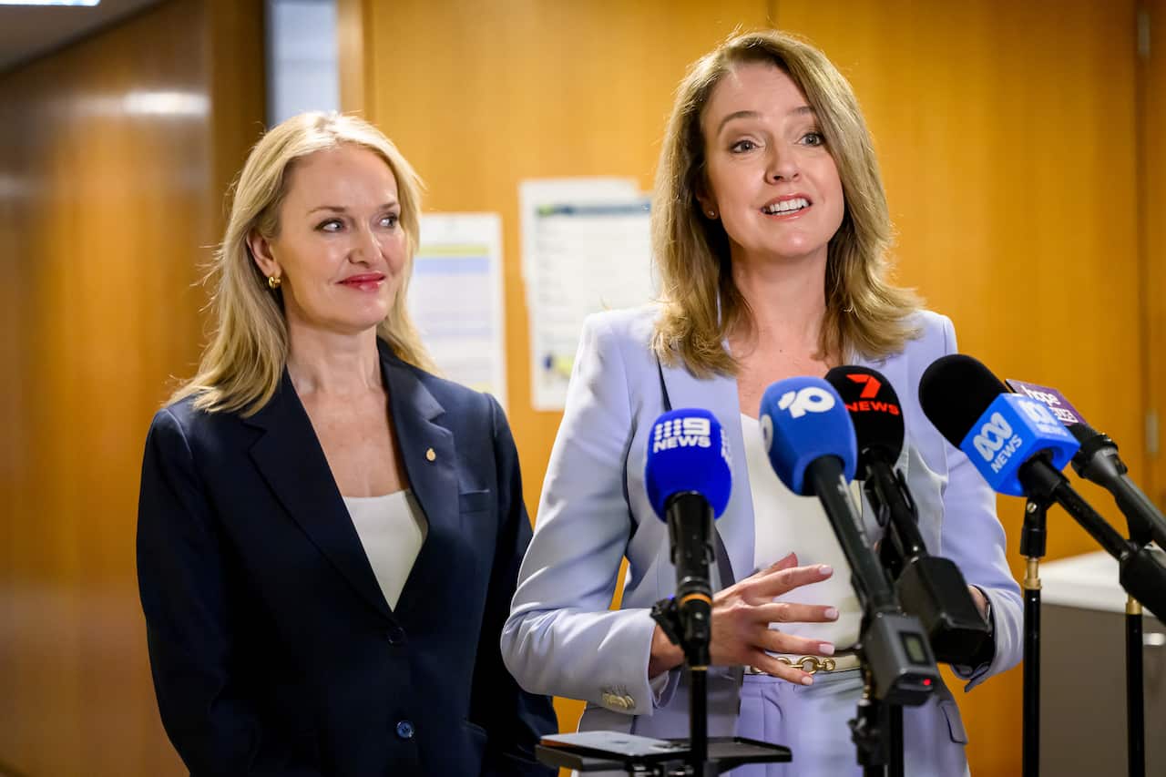 A woman on the left with blonde hair and a navy jacket, and a woman on the left in a lavender jacket.