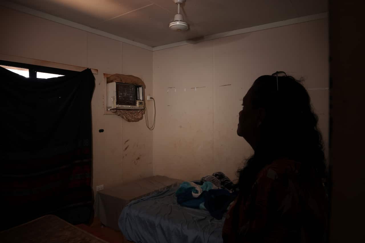 A silhouette of a woman looking towards an air-conditioning unit with the ceiling fan running.