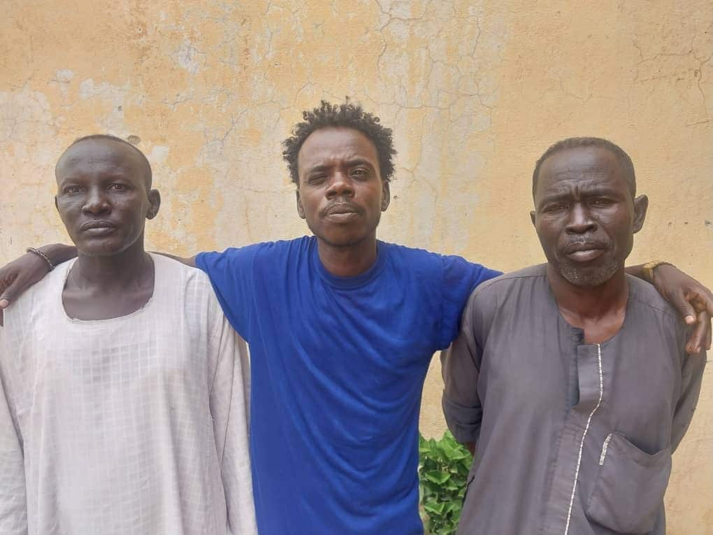 Three men standing against a wall.