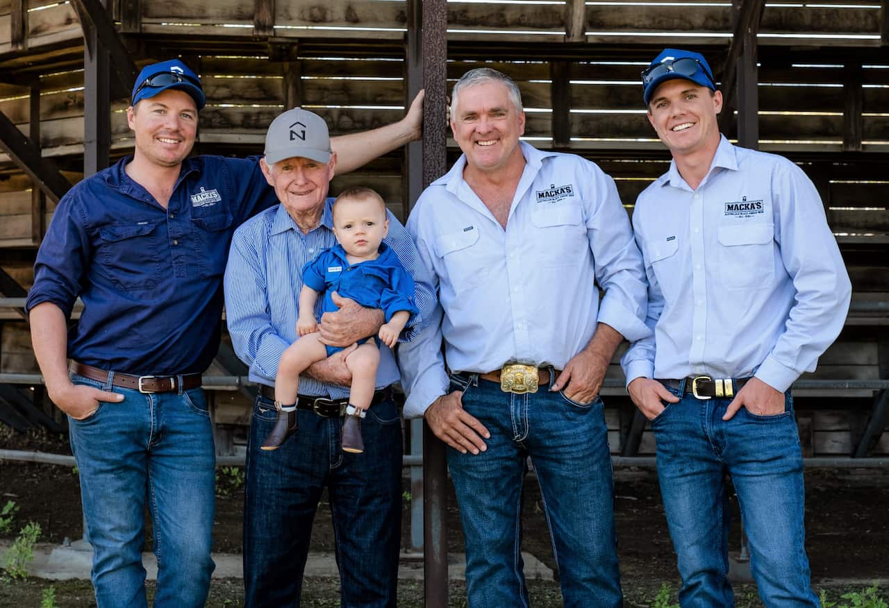 A group of men in blue shirts stand in a row, with an older man holding a young child.