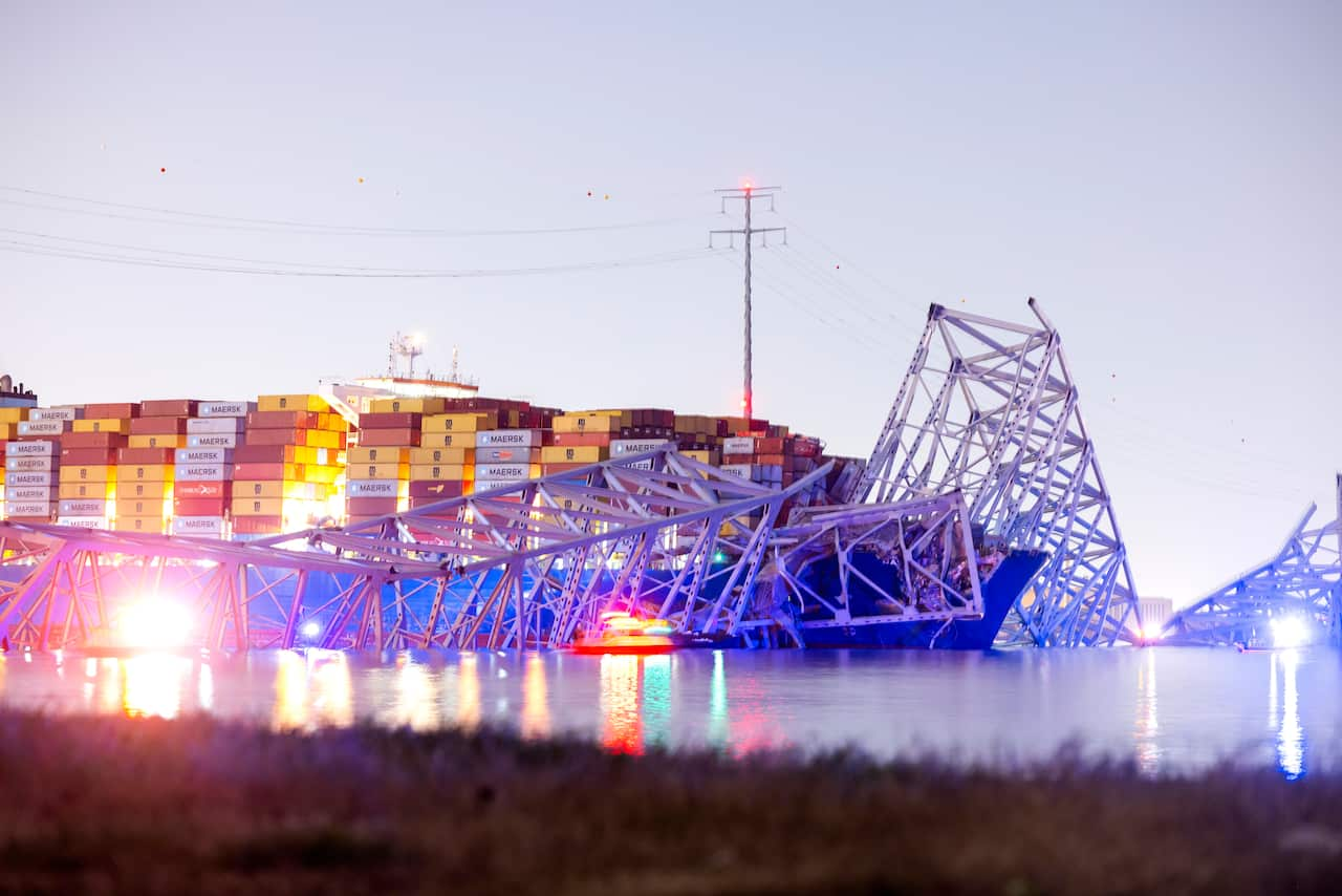 A container ship with collapsed sections of a metal bridge laying over the bow. 