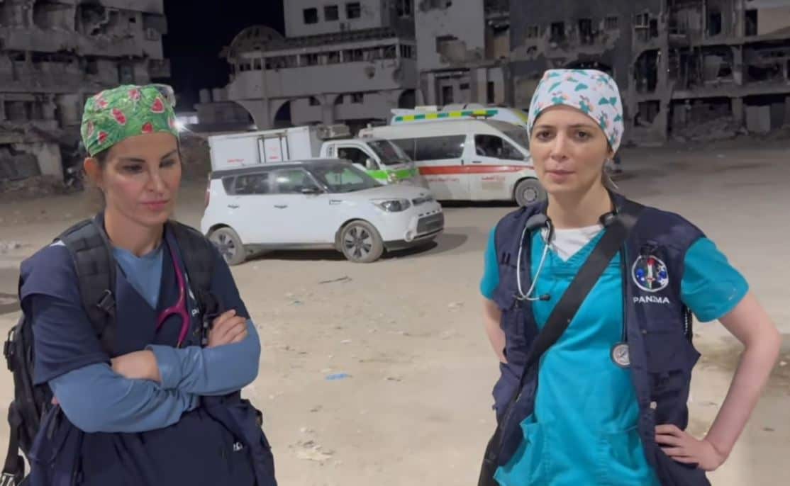 Two doctors in scrubs surrounded by damaged buildings.