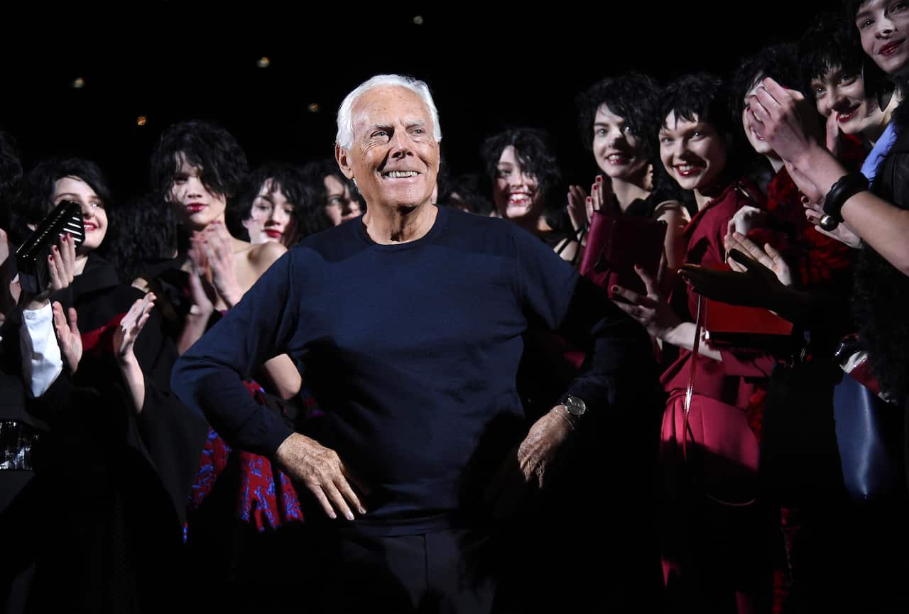 A fashion designer poses with models at the end of his collection show as the spectators clap.