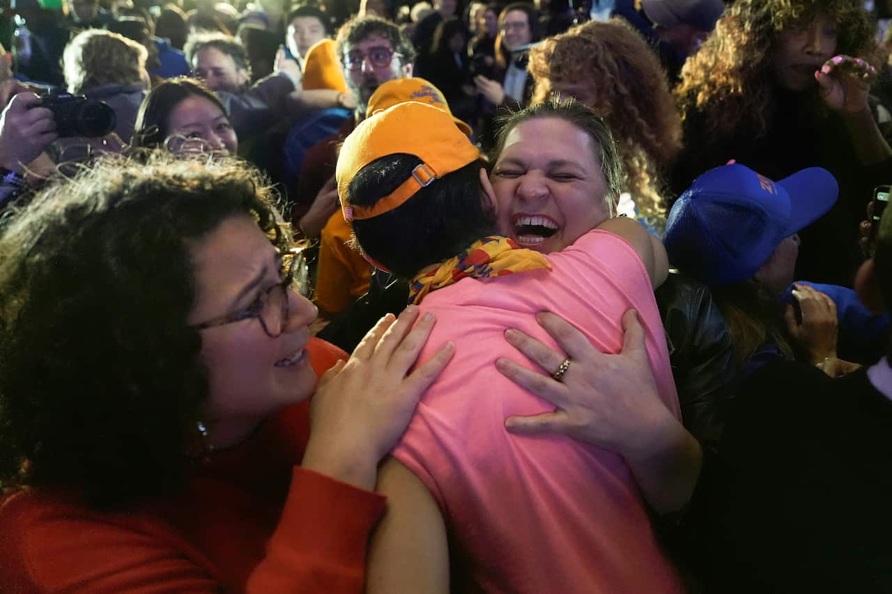 A person in a pink shirt hugs a woman in a crowd