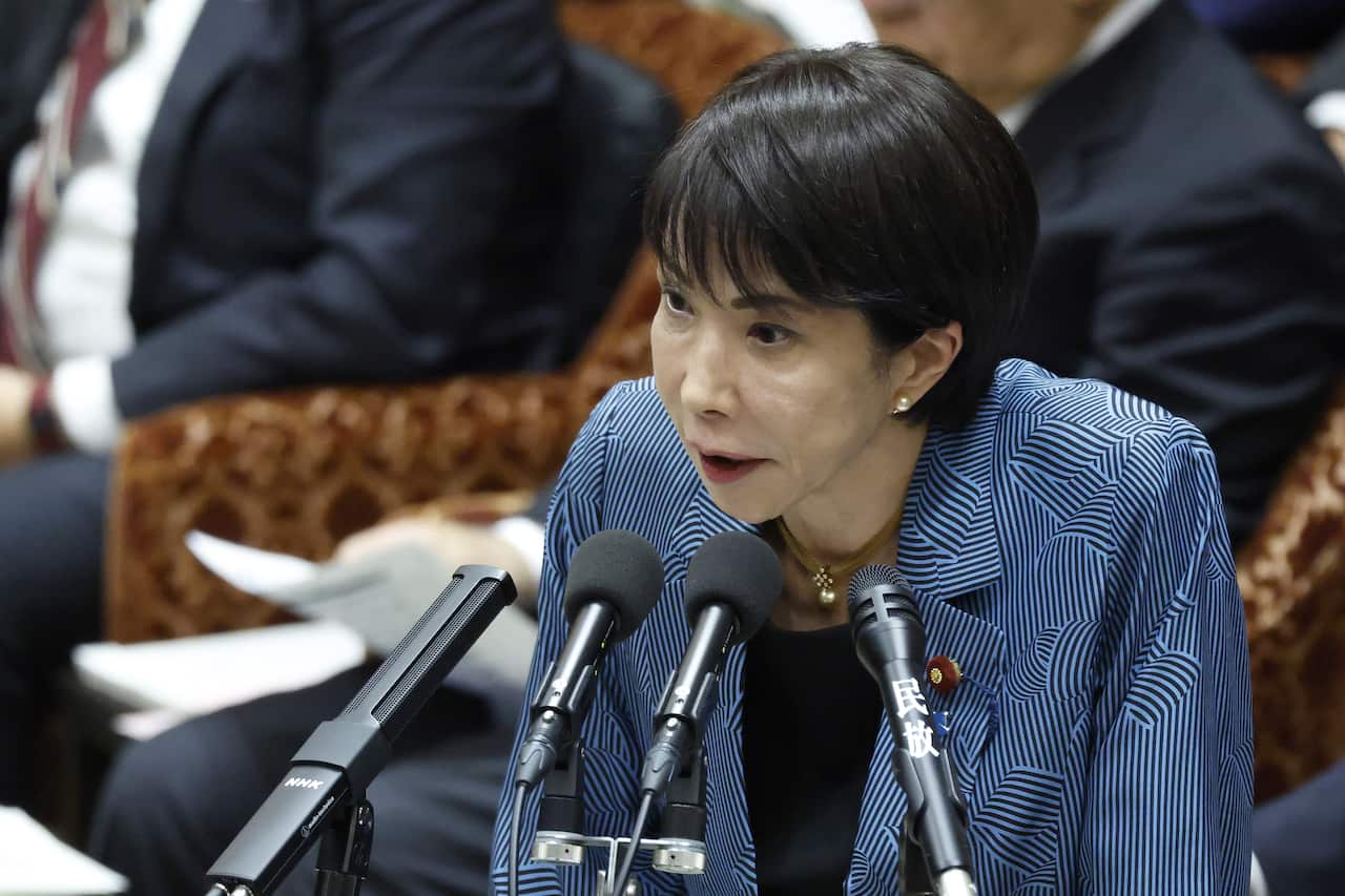 Sanae Takaichi speaking into a microphone in a parliamentary setting.