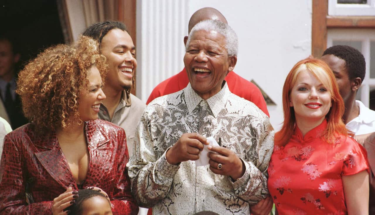 Two women dressed in red smile while Nelson Mandela stands between them and laughs