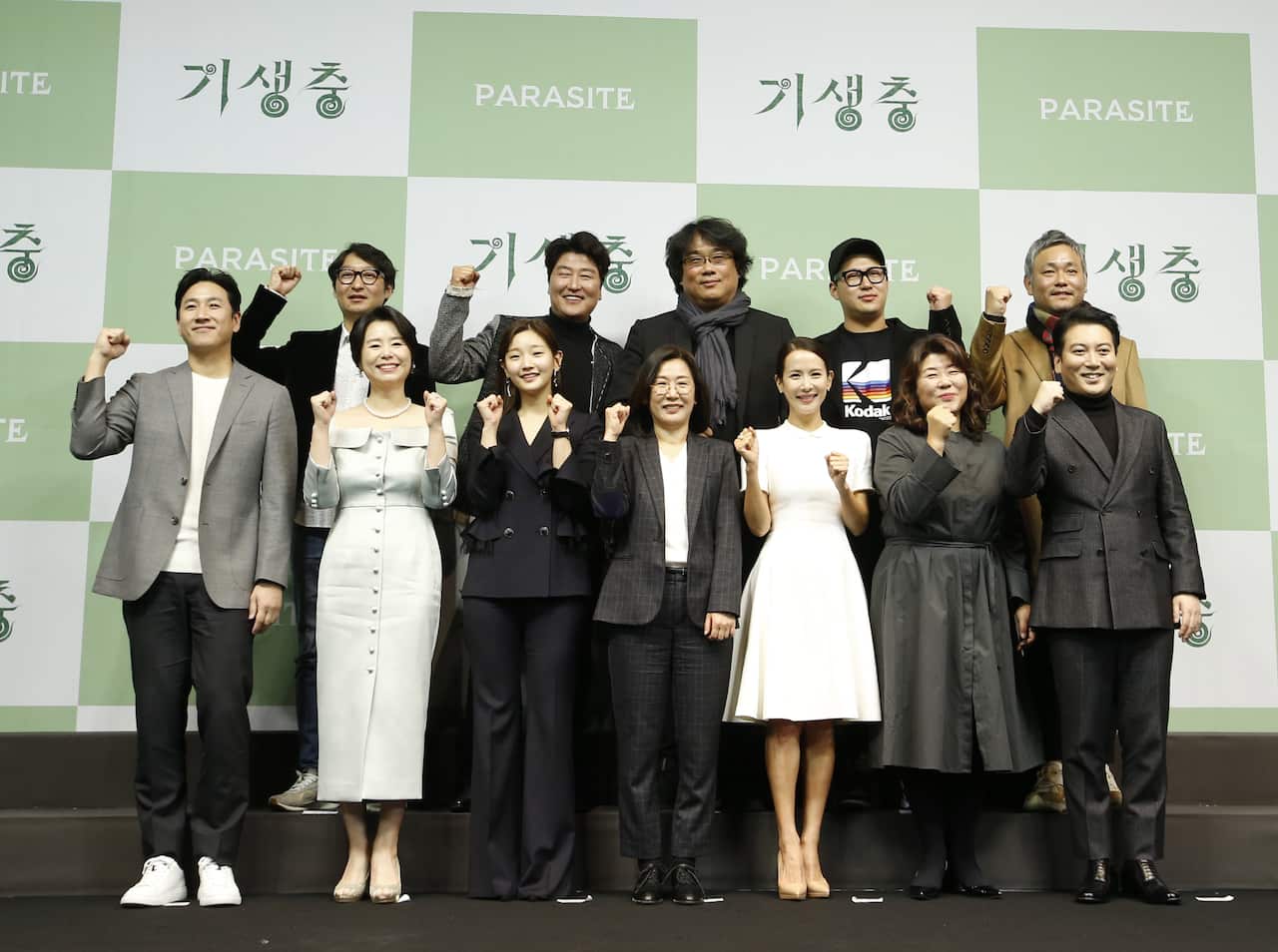 Two rows of people smiling, standing in front of a large green and white banner.