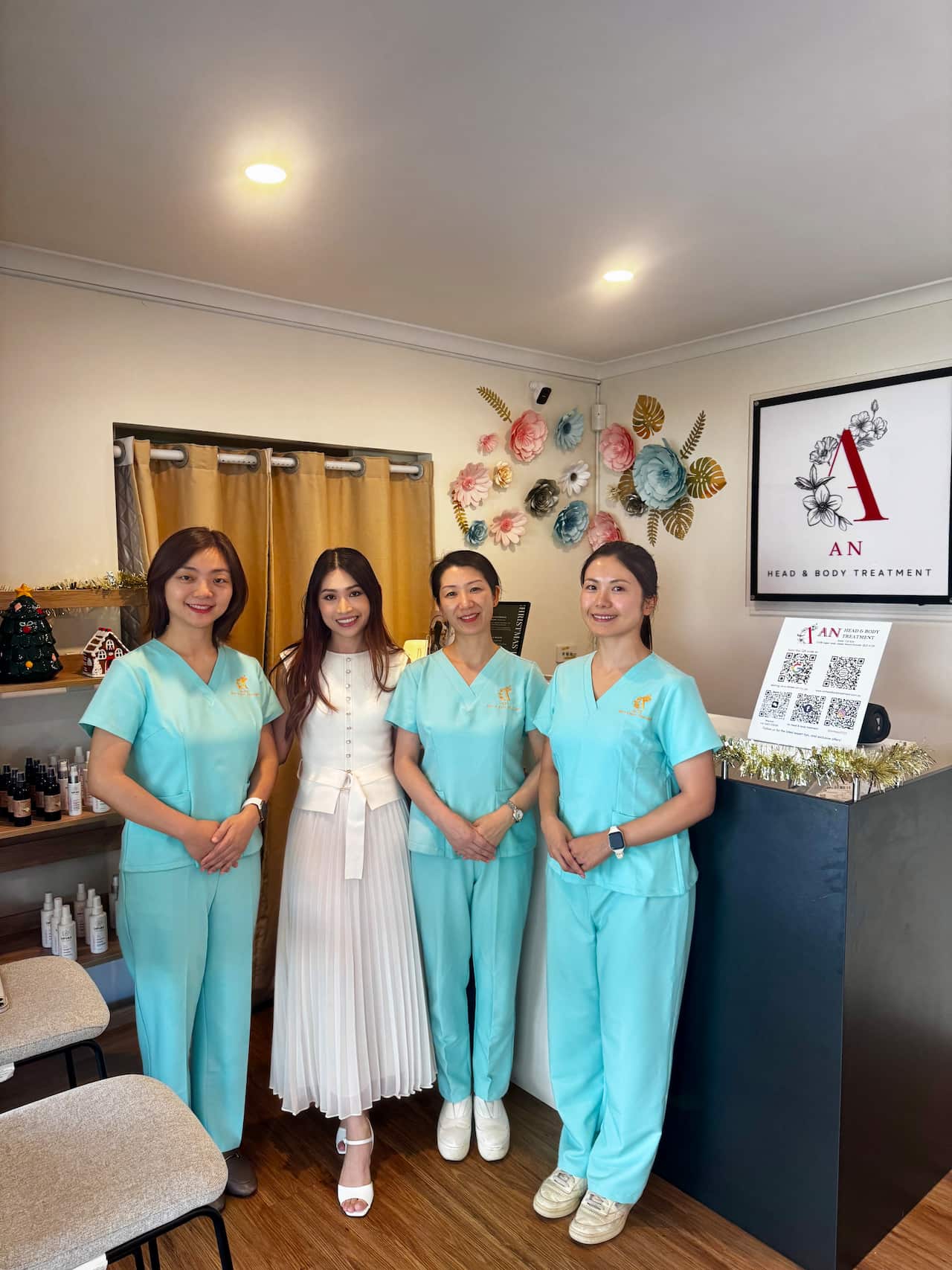 Três mulheres de uniforme azul e uma de vestido branco sorrindo dentro de um spa de bem-estar