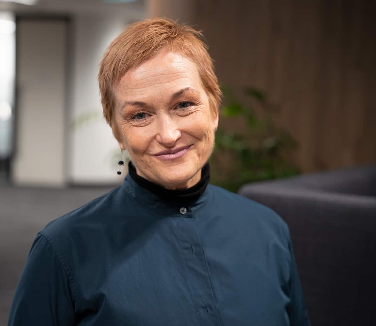 A woman in a blue top stands smiling at camera.