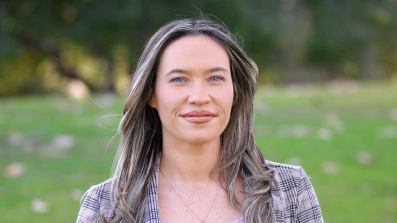 Closeup shot of a woman with long, dark blonde hair and blue eyes in a tartan blazer in a field