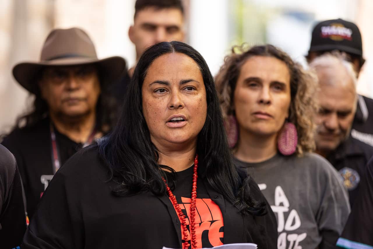 A group of people, with one woman with black hair in the centre, speaking.