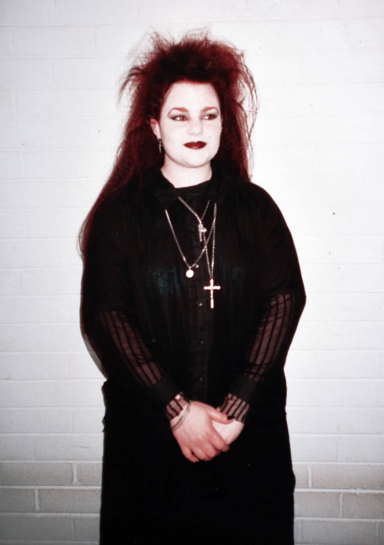 A woman with teased long red hair and gothic makeup in black gothic clothes and silver necklaces