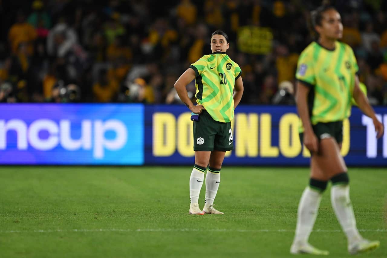 Two football players stand on the pitch wearing yellow and green jerseys