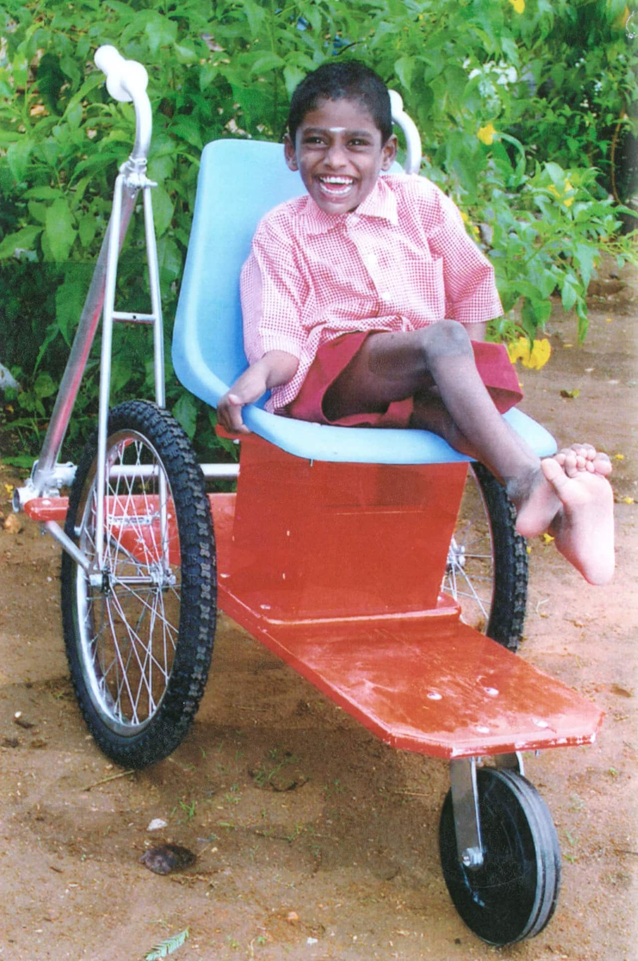 A child with a big smile sits on a wheelchair with a bright blue seat.