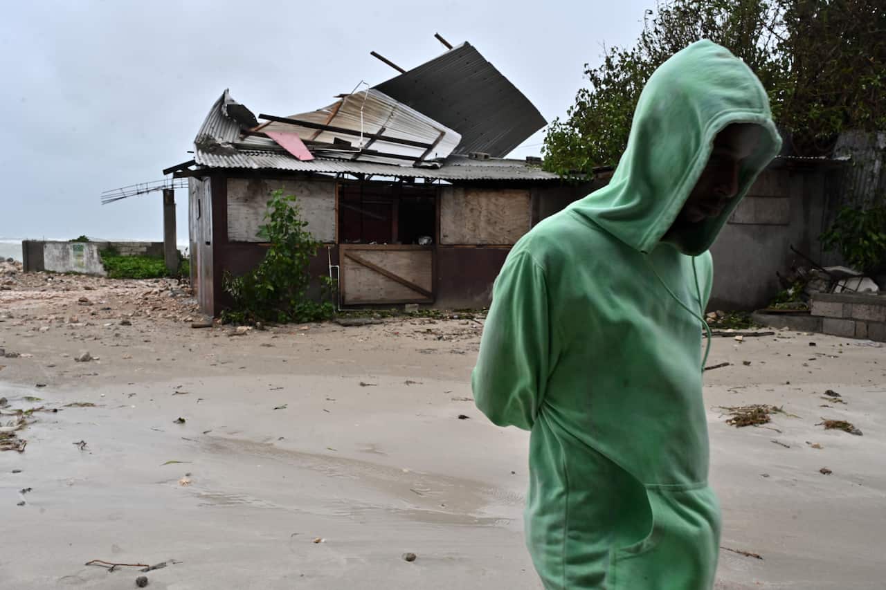 A man walks by a house damaged by the preliminary winds of Hurricane Melissa at Hellshire Fishing Beach in Portmore, Jamaica
