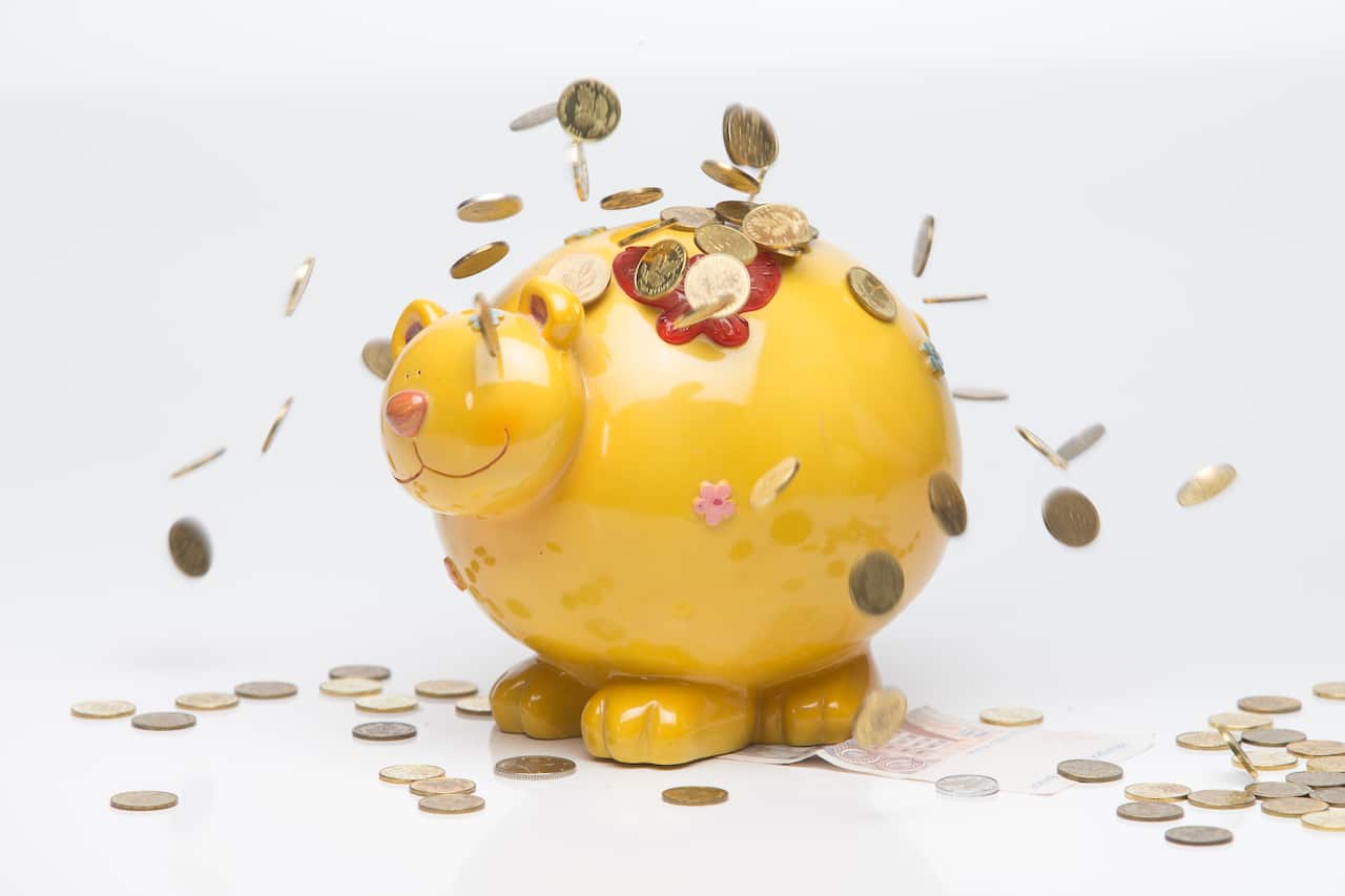 A yellow piggy bank with coins dropping on it