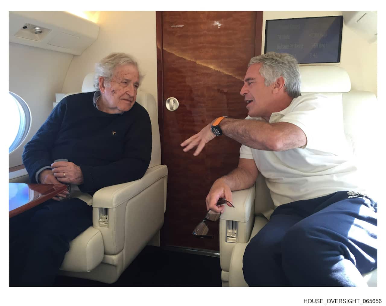 Noam Chomsky and Jeffrey Epstein are seated across from each other in cream-colored leather seats on a private jet, engaged in conversation.