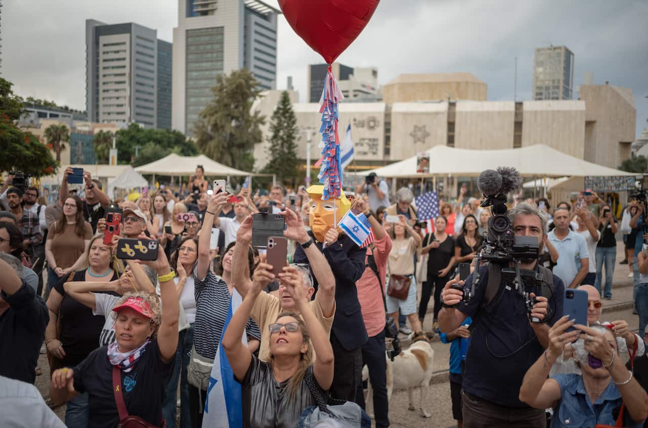 A group of people, some carrying Israeli and American flags, hold up their phones at an outdoor celebration.