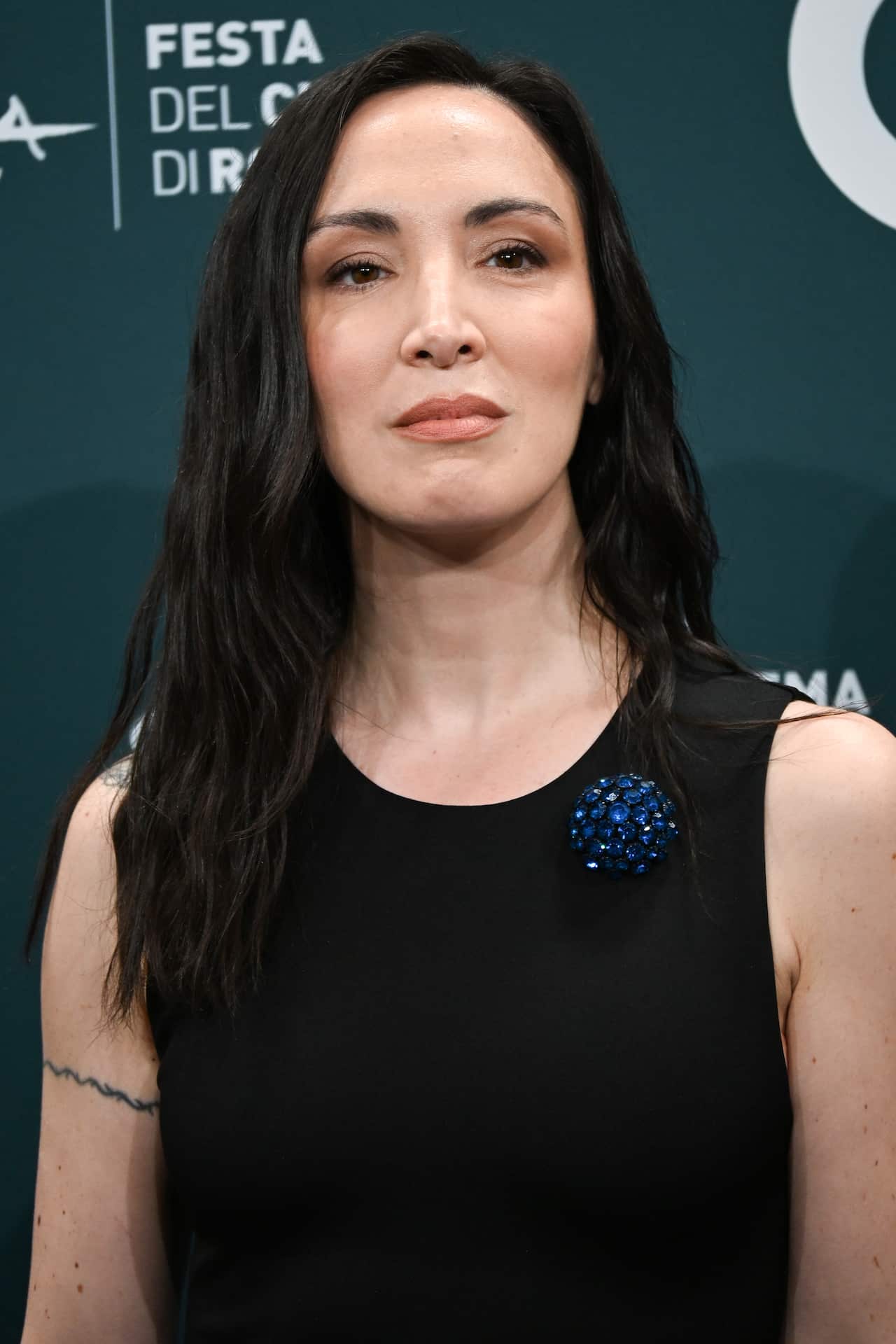 A woman with dark hair and a dark dress posing in front of a media wall.