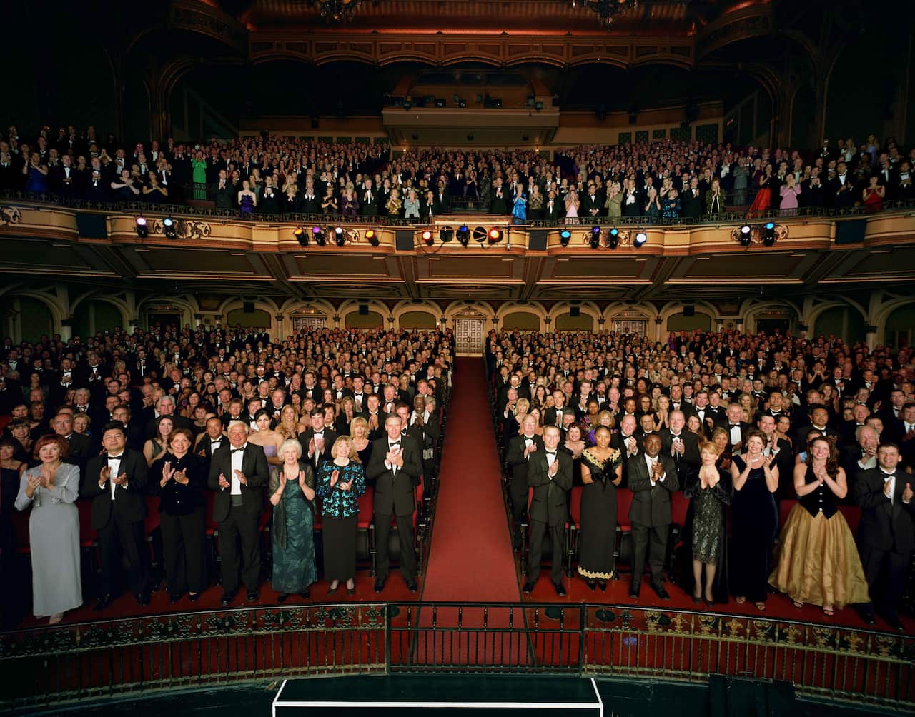 Theater audience standing in formal attire, applauding