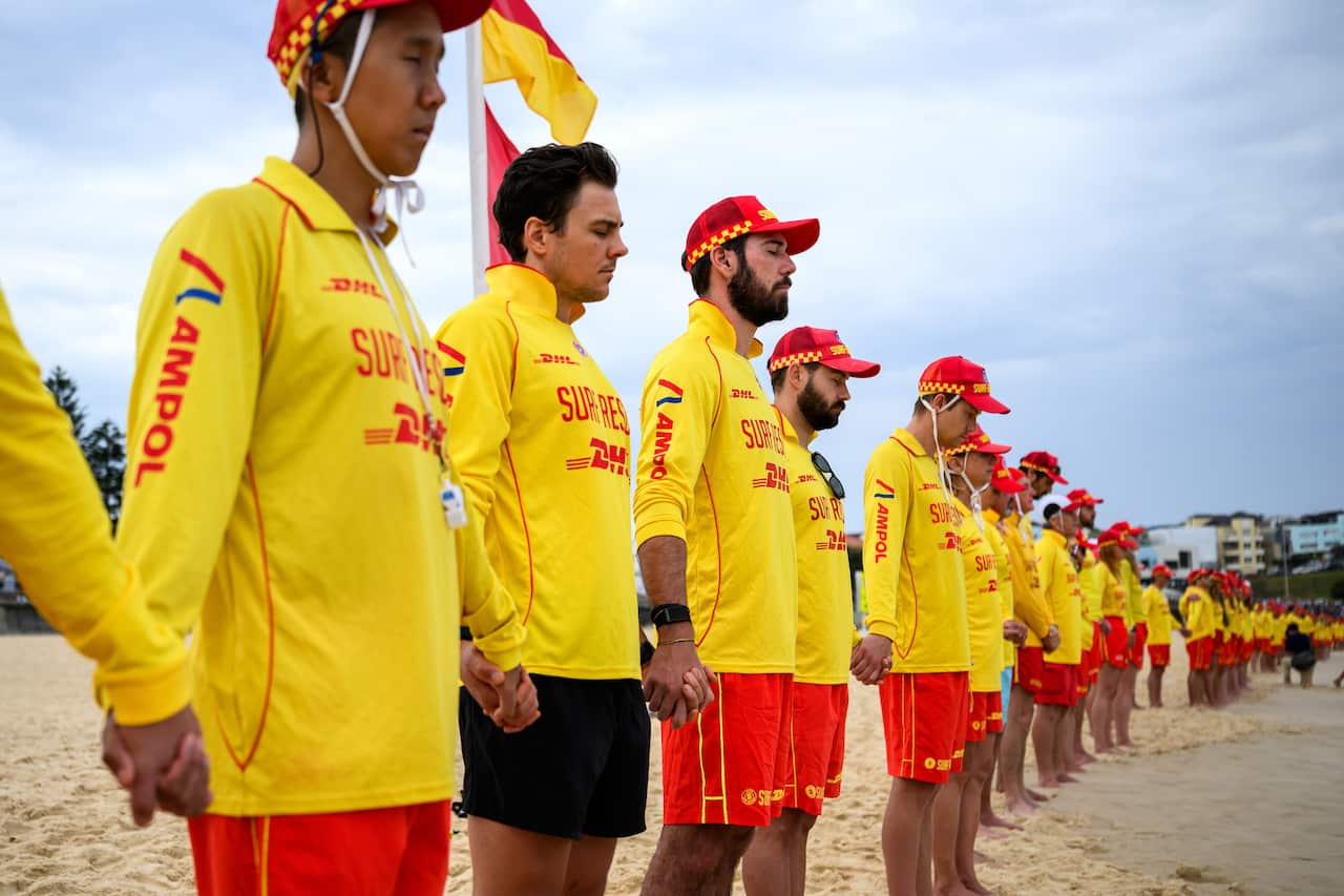 Los salvavidas vestidos de amarillo forman fila en la playa y se toman de la mano.