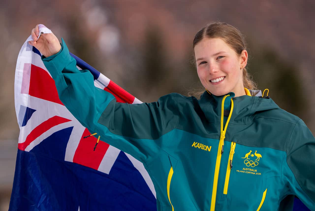 Una joven viste un chándal verde con cremalleras amarillas y sostiene una bandera australiana.