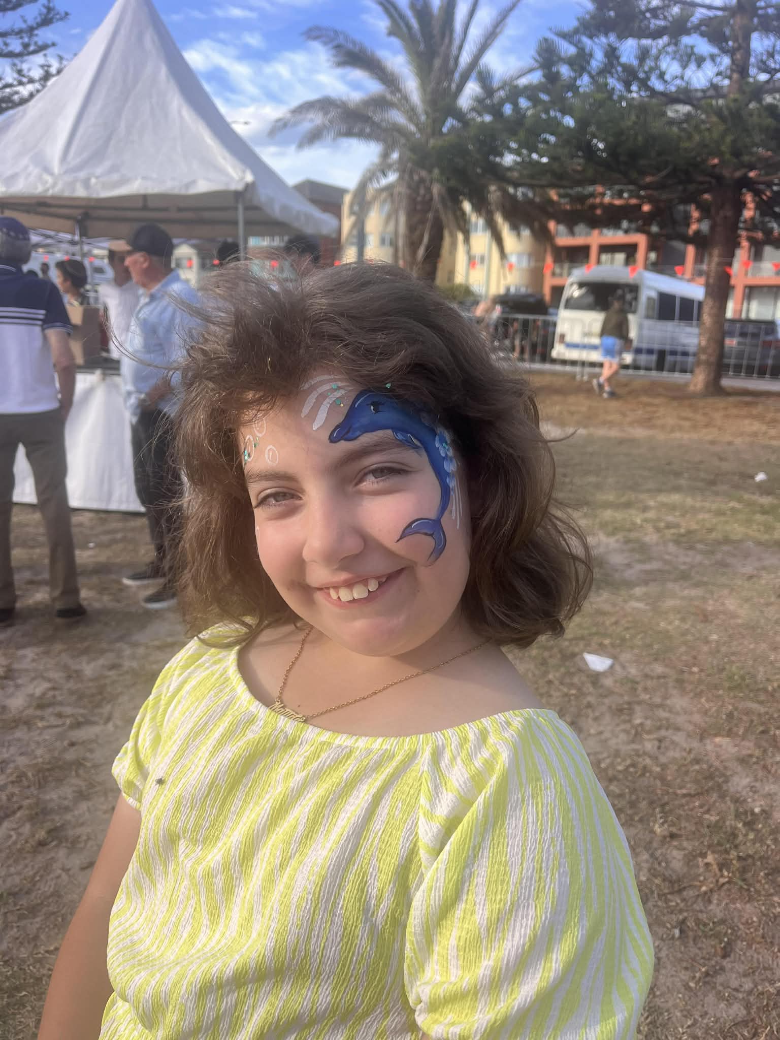 A girl whose face has been painted with an image of a dolphin smiles into the camera