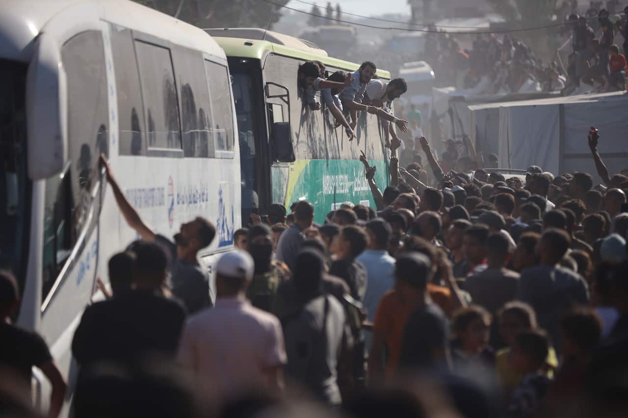 A large crowd of people standing outside two buses. Some people are waving from one of the buses' windows.
