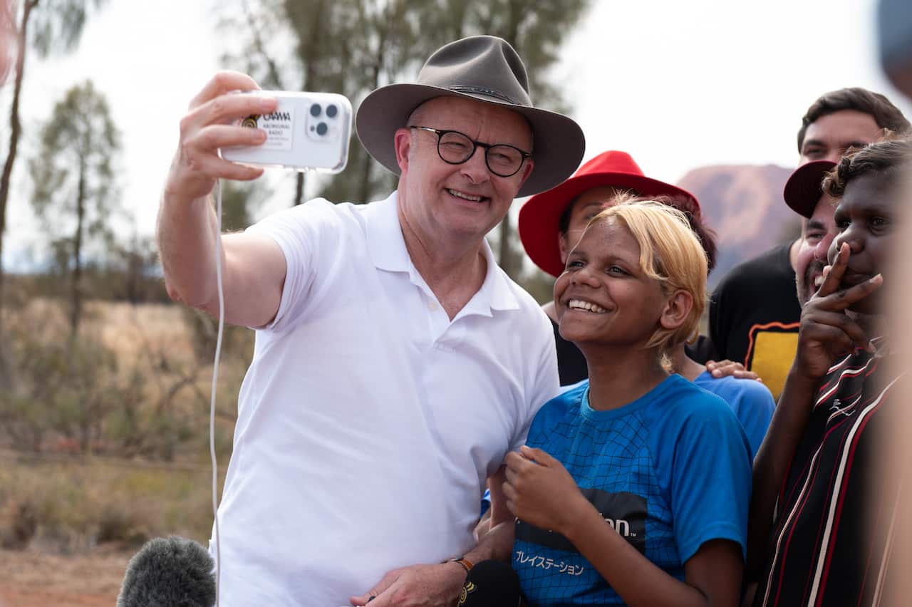 Wearing a white shirt and a broad-brimmed hat, prime minister Anthony Albanese takes a selfie with a young Indigenous girl.