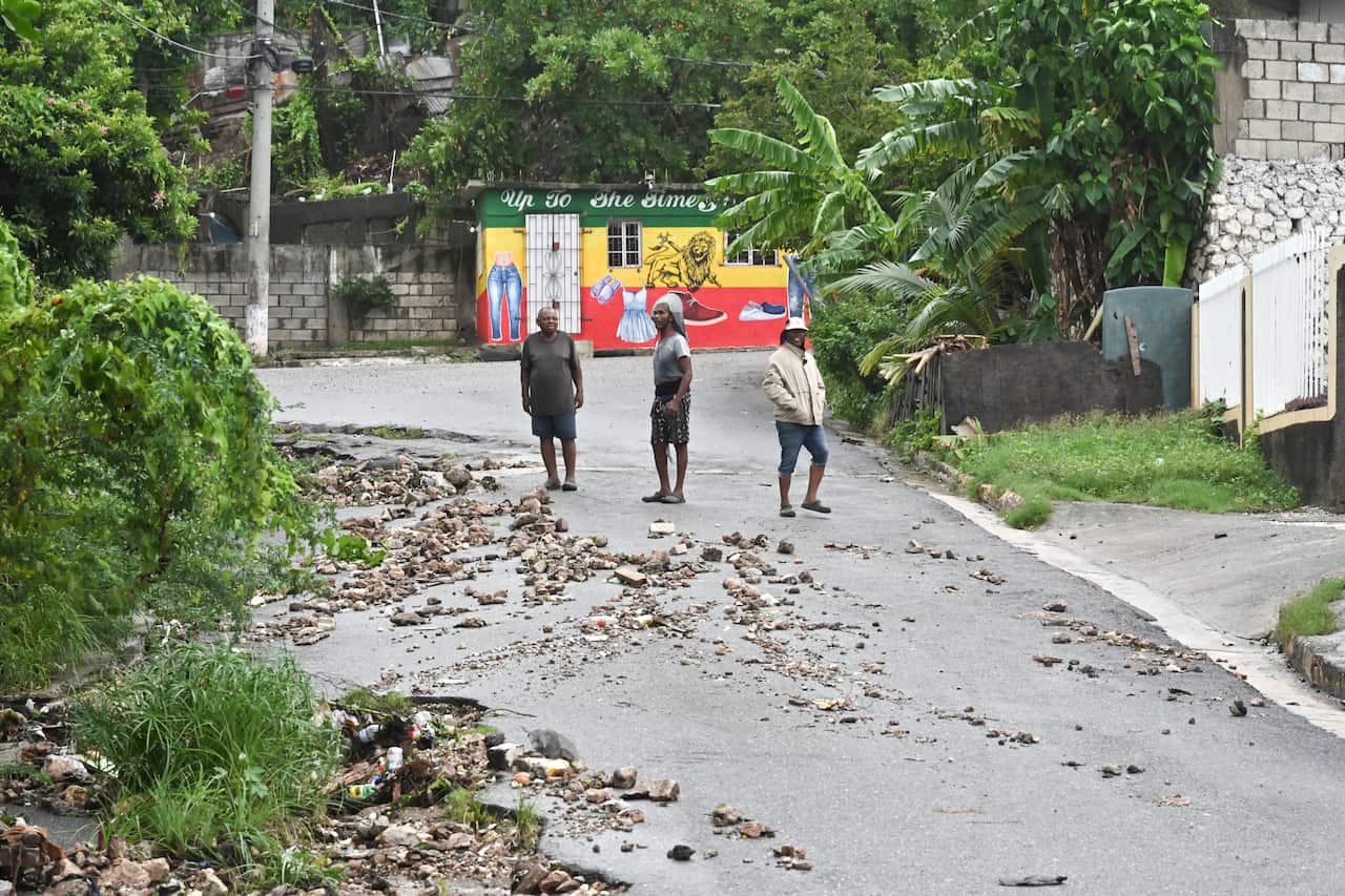 Three people stand on a road covered with debris and fallen trees.