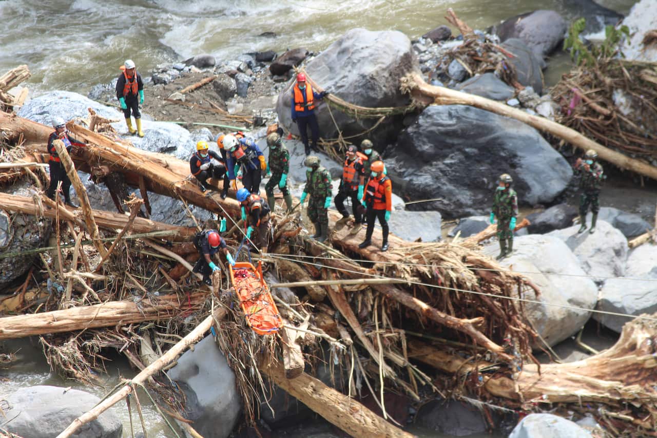 Emergency workers stand on a makeshift bridge made with fallen trees amid rocks as they carry out rescue work.