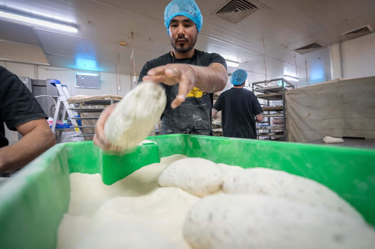 A man holding a raw bread loaf inside a bakery.