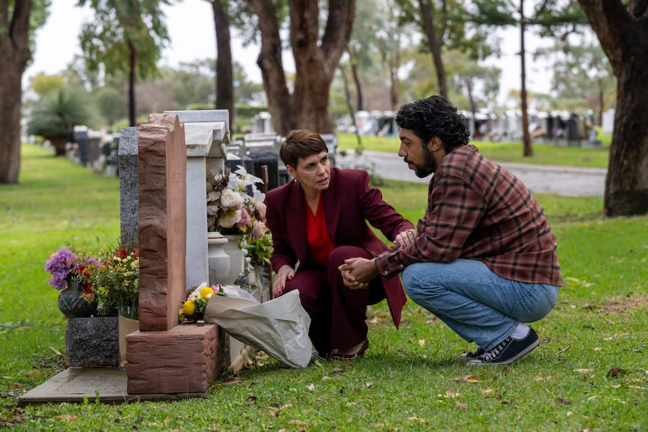 Two people kneeling down in front of a gravestone. 
