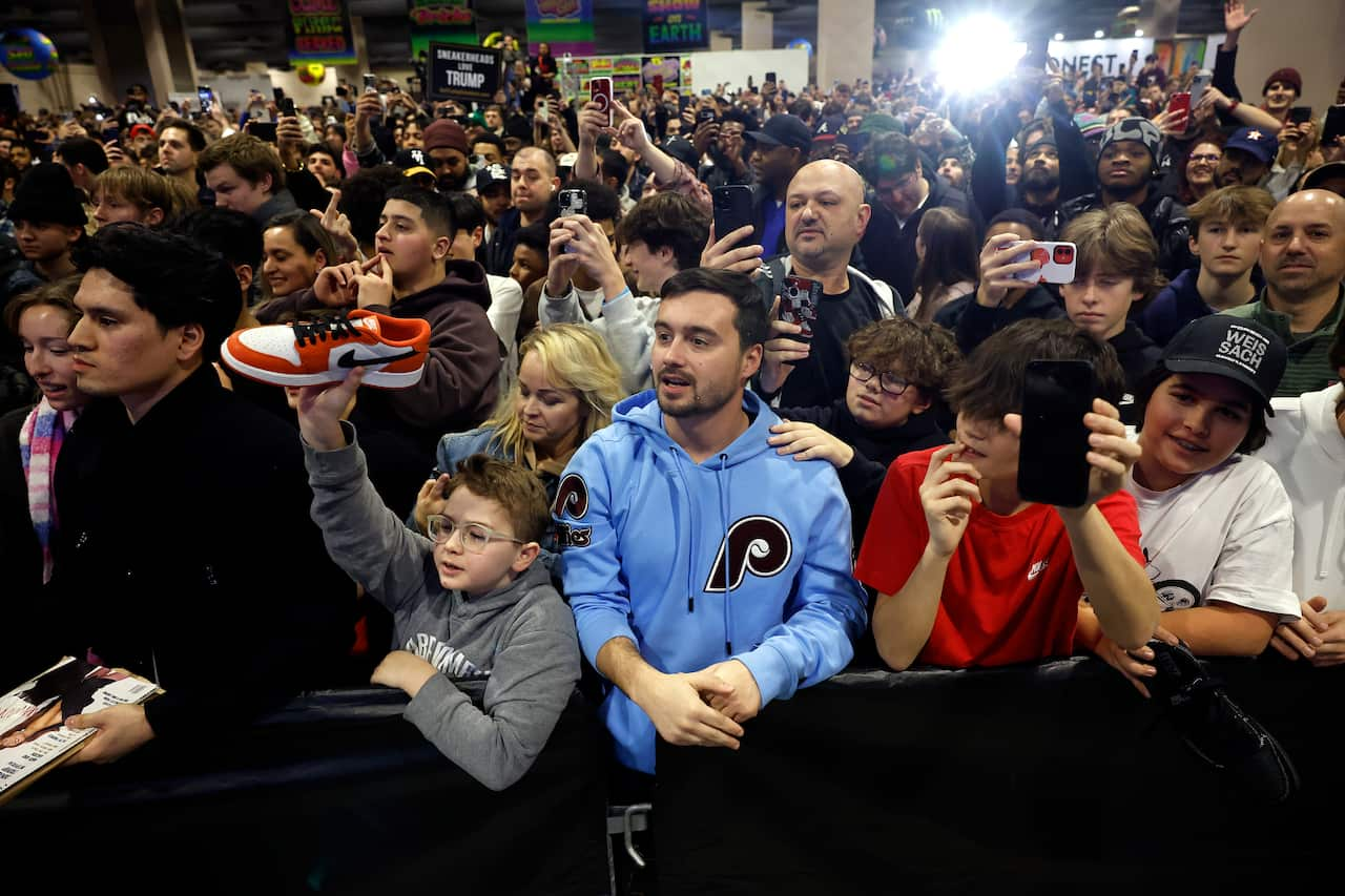 A crowd of people standing indoors. Some are taking photos, others are holding placards.