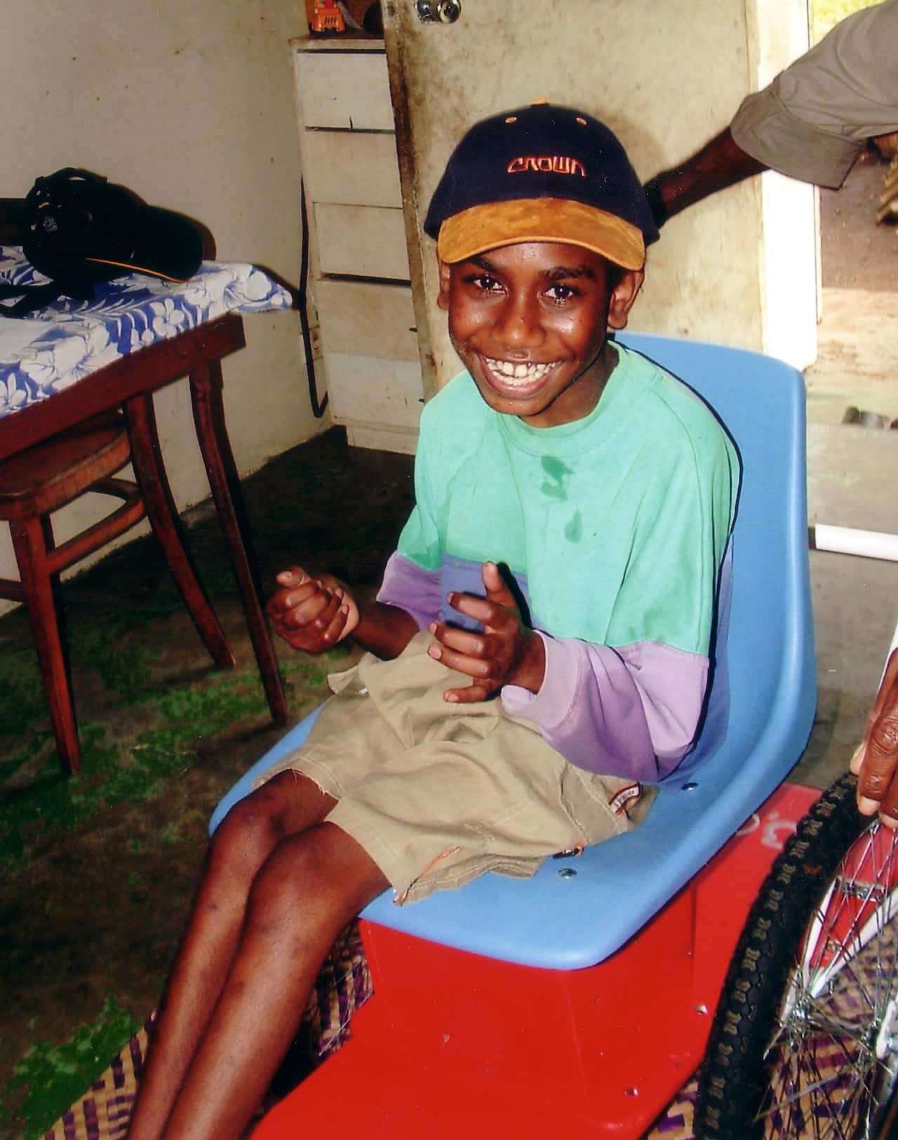 A young boy sitting in a wheelchair smiles for the camera.